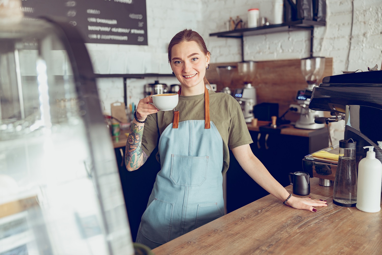 Joyful Female Barista With Cup Of Coffee Working In Cafe – ©Adobe Stock